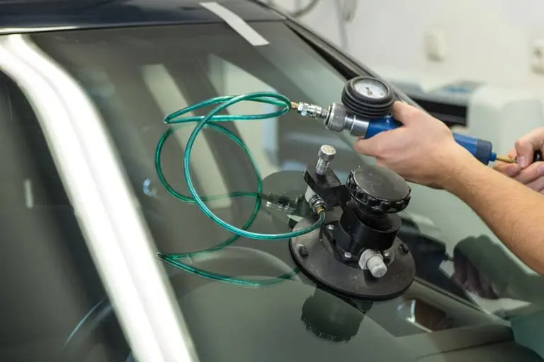 Man in green apron repairing damage on car windshield