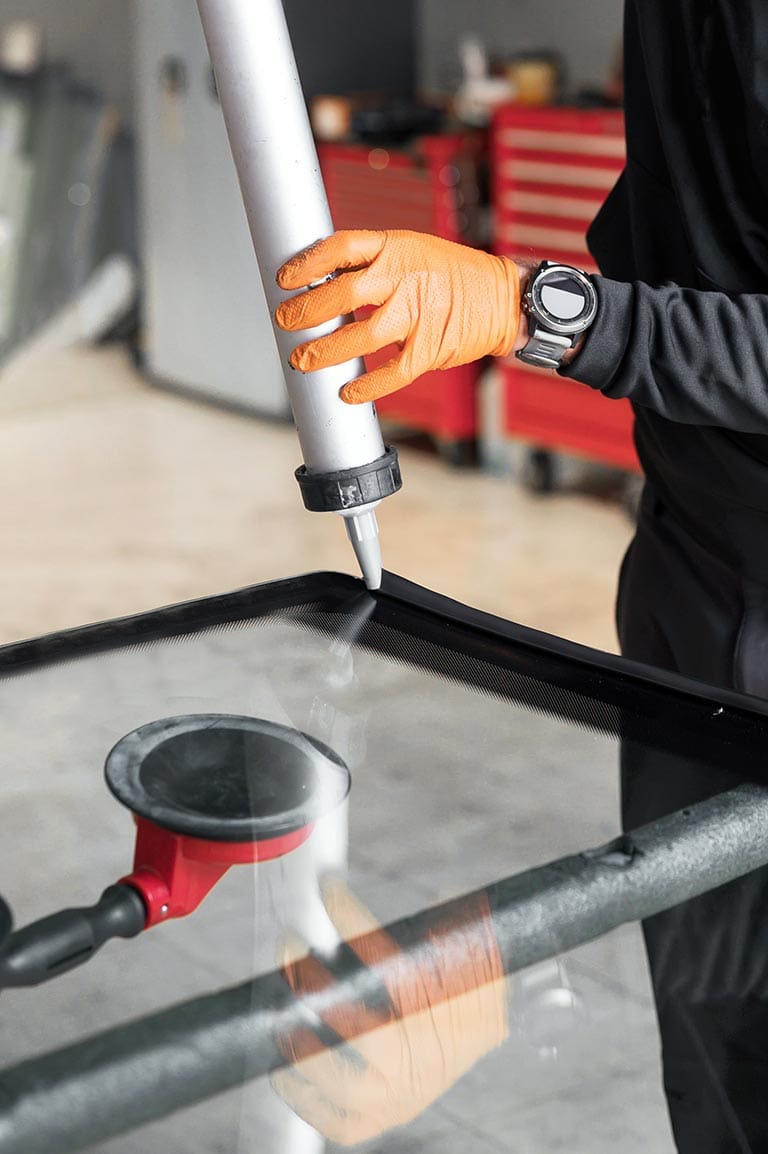 Glazier applying rubber sealing to windshield in garage, close up. High quality photo