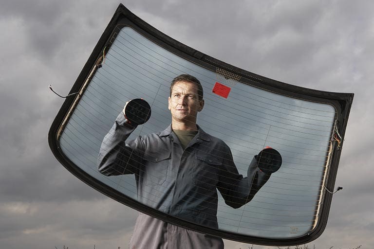 Car mechanic holding rear windscreen with suction pads